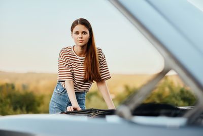 Portrait of young woman standing in car