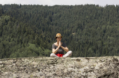 Full length of young woman sitting on mountain rock formation