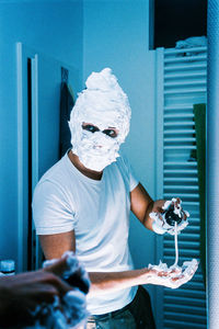 Portrait of man holding camera while standing at home