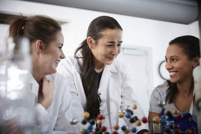 Smiling mature chemistry teacher with young female students in classroom at university
