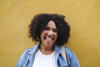 Happy young woman with curly hair in front of yellow wall