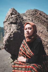 Woman looking away while sitting on rock