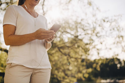 Low angle midsection of woman wearing headphones while mobile phone in summer