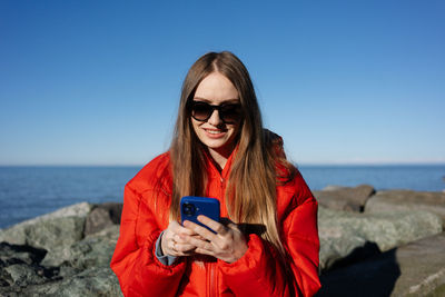 Young woman using mobile phone while standing against sea