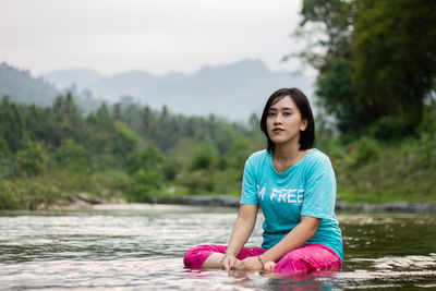 Portrait of smiling woman sitting on lake against trees