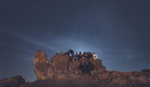 Low angle view of people on rock formation against sky