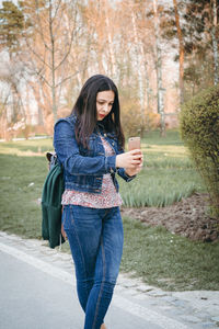 Full length of young woman using phone while standing on tree