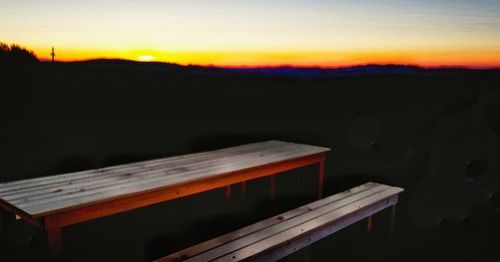 Empty bench on field against sky during sunset