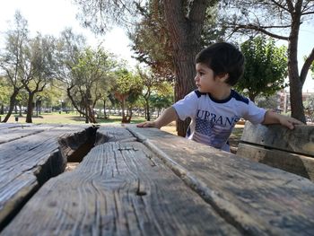 Boy sitting on old wooden bench at park