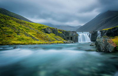 Scenic view of waterfall against cloudy sky