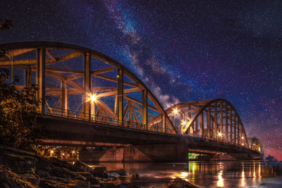 Illuminated bridge over river against sky at night