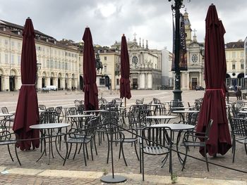 Chairs and tables at sidewalk cafe against buildings in city