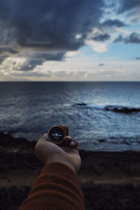 Cropped hand of person holding seashell at beach against sky