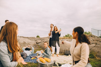 Happy male and female friends having fun on field against sky during picnic