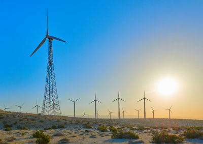 Wind turbines on field against sky during sunset