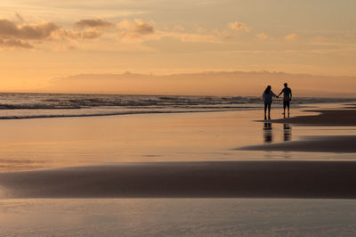 Silhouette men standing on beach against sky during sunset