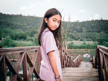Portrait of cute girl standing by railing on footbridge