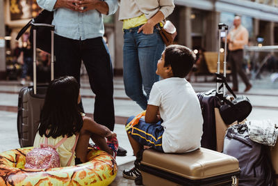 Children listening to parents while waiting with luggage at railroad station