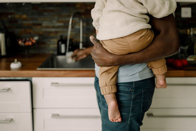 Midsection of father carrying baby boy while doing chores in kitchen