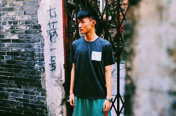 PORTRAIT OF YOUNG MAN STANDING ON WALL
