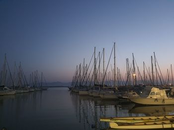 Sailboats moored in harbor at sunset