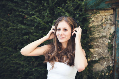 Young woman smiling and listening to music via headphones outdoors