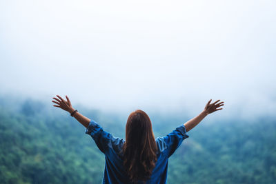 Rear view of a female traveler open arms and looking at a beautiful green mountain on foggy day