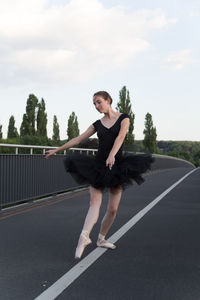 Female ballet dancer dancing on bridge against sky