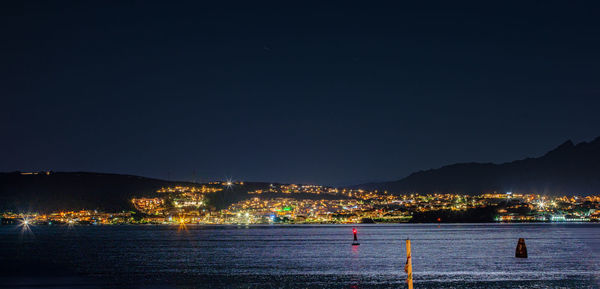 Illuminated city by sea against clear sky at night