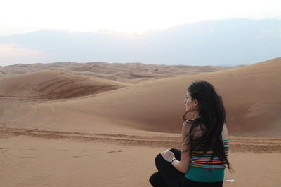 Woman standing on sand dune in desert against sky