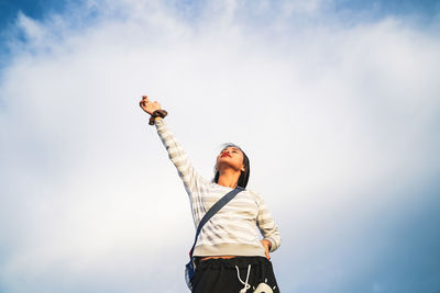 Low angle view of woman with hand raised standing against cloudy sky