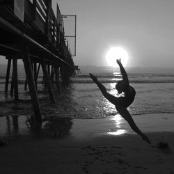 Silhouette woman dancing at beach by pier during sunset