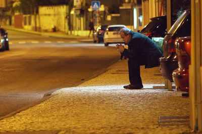 Full length of man sitting on footpath at night