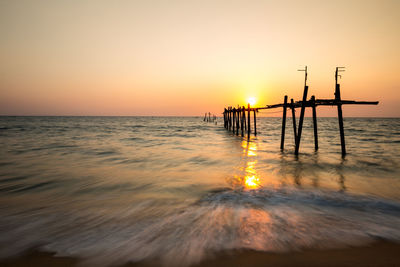 Silhouette wooden posts on beach against sky during sunset
