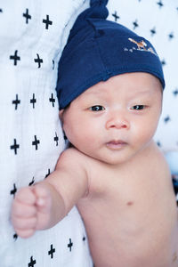 Close-up of shirtless baby wearing cap while lying on bed