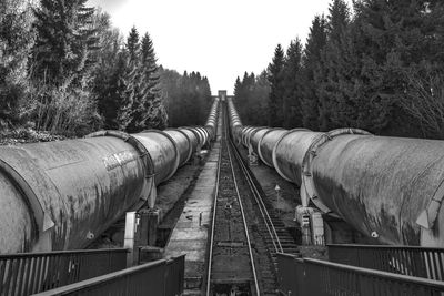 Railway tracks amidst pipes and trees against sky