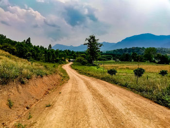 Dirt road along landscape and mountains against sky