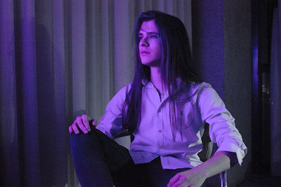 Man with long hair looking away while sitting on sofa