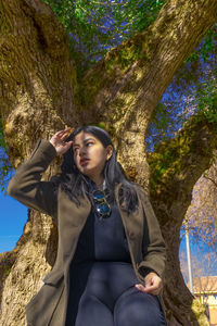 Portrait of young woman sitting against trees