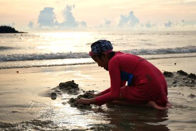 Girl playing with sand against sea during sunset