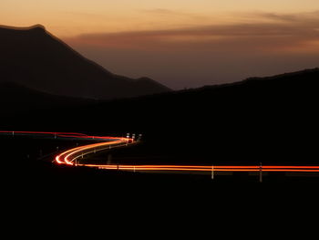 Silhouette of volcanic landscape against sky during sunset with road a taillight trails