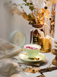 A cup of milk tea with rosebud on top beside yhe window with sunlight