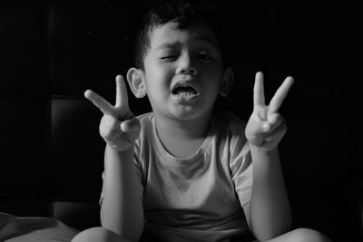 Close-up portrait of boy showing peace sign while sitting in darkroom