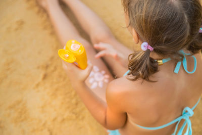 High angle view of girl with suntan lotion sitting on beach