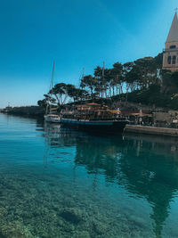 Sailboats moored on sea against clear blue sky