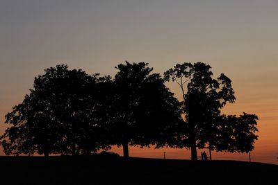 Silhouette trees on field against sky during sunset