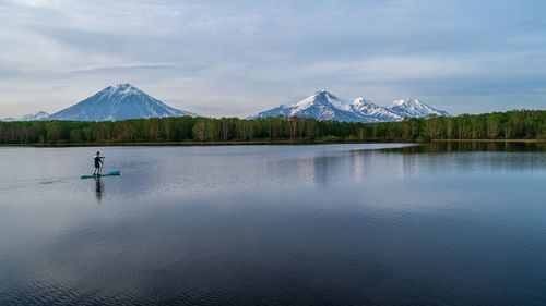 Man paddleboarding in lake by mountains against sky