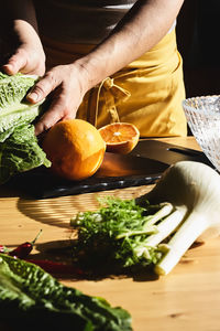 Woman cuts an orange on the cutting board and prepares lettuce, fennel and orange salad. 