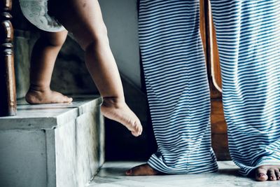 Low section of baby girl moving down steps while mother standing at home