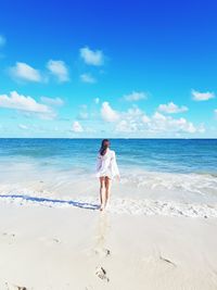 Full length rear view of woman walking towards sea on shore at beach against sky